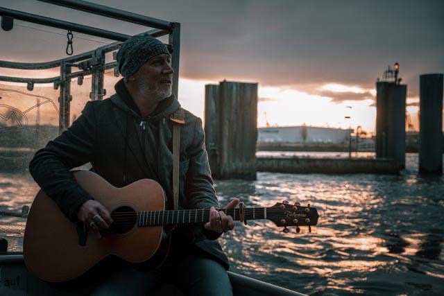 Thias spielt Gitarre auf einem Boot im Hafen bei Sonnenuntergang.