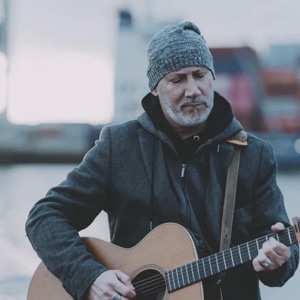 Cover: Thias mit Strickmütze spielt Akustikgitarre am Hafen.