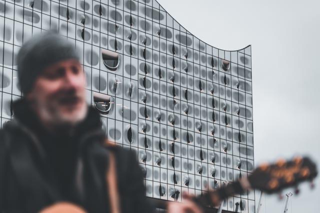 Thias mit Gitarre unscharf im Vordergrund, dahinter die Fassade der Elbphilharmonie.