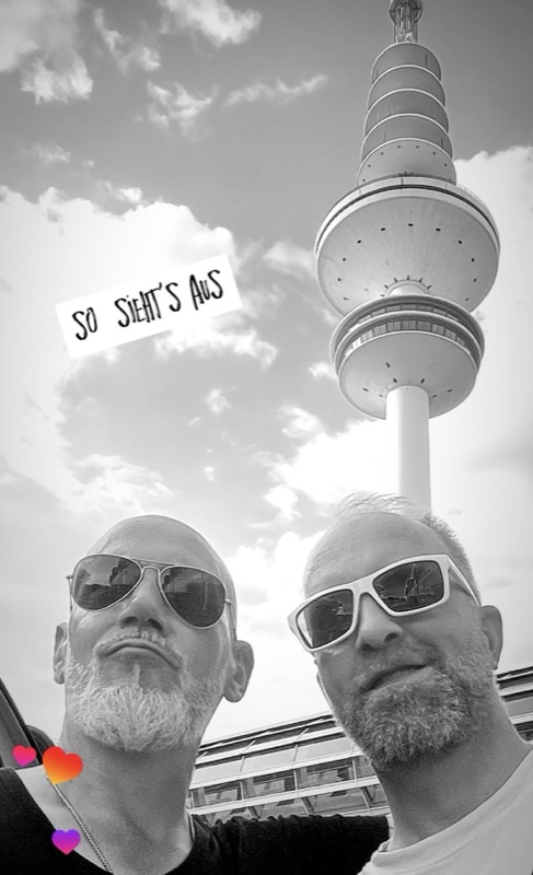 Schwarz-Weiß-Selfie: Thias und Charlante mit Sonnenbrillen vor dem Fernsehturm, daneben der Schriftzug „So sieht’s aus“.