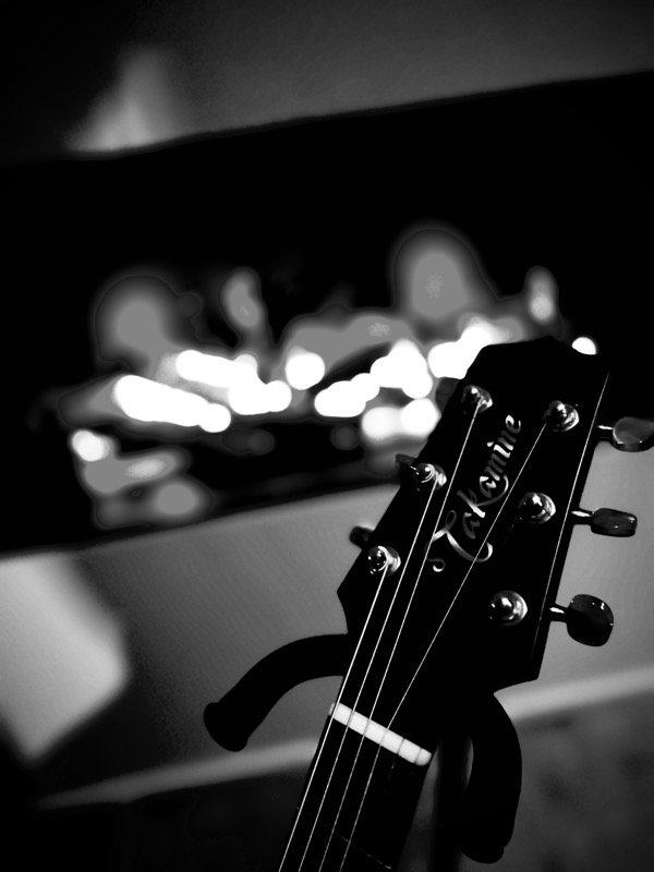 Schwarz-Weiß-Detail: Kopfplatte einer Akustikgitarre vor unscharfen Lichtern.
