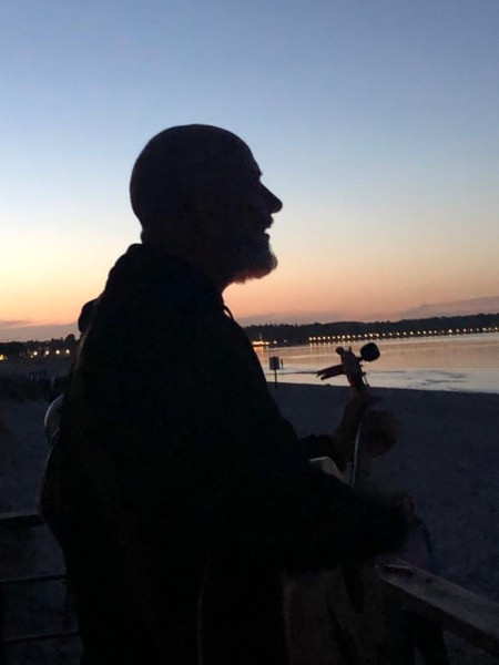 Silhouette im Profil mit Instrument vor dem Abendhimmel am Wasser.