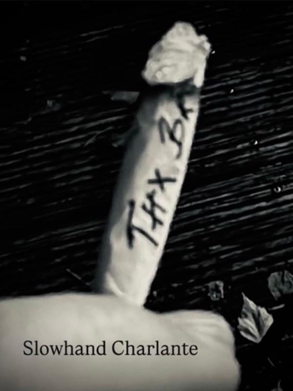 Schwarz-Weiß-Detail: eine selbstgedrehte Zigarette mit der handschriftlichen Aufschrift „Thx B…“ auf dunklem Holz, darunter der Schriftzug „Slowhand Charlante“.