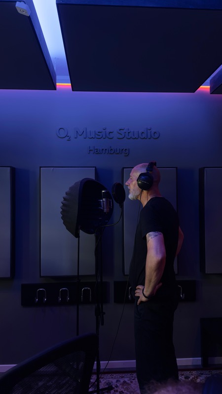 Thias mit Kopfhörern vor dem Mikrofon in einem Aufnahmestudio, violettes Licht.