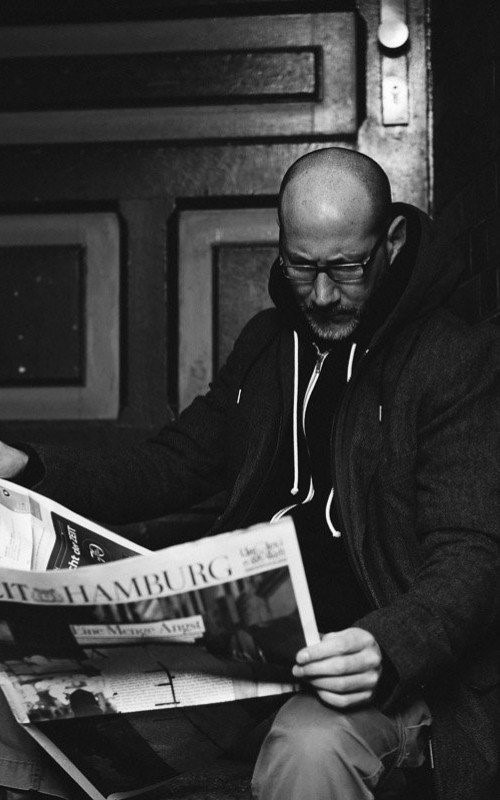 Schwarz-Weiß-Foto: Thias liest in einem Hauseingang eine Zeitung.